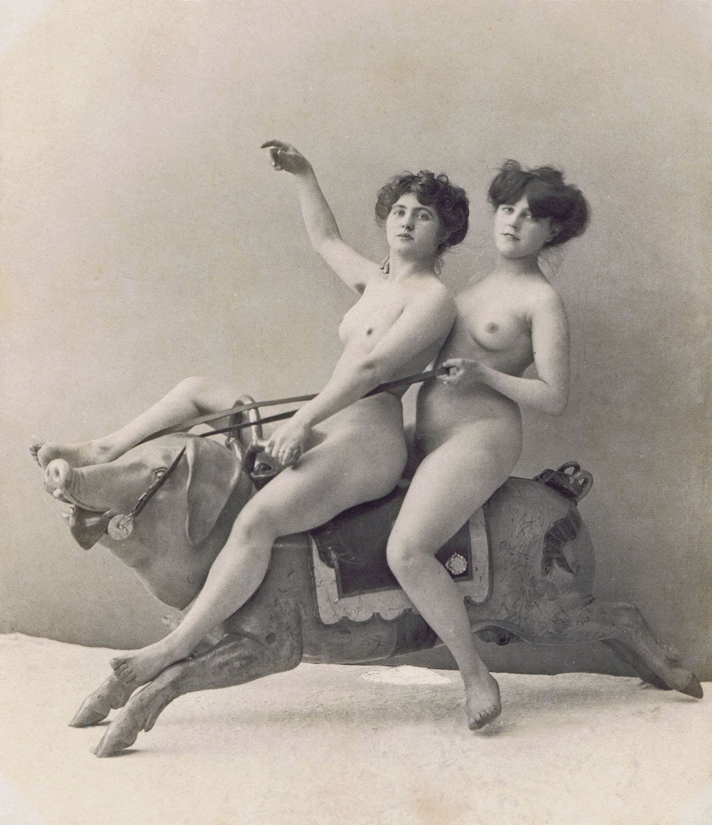 Two nude women on a carousel pig, around 1900.